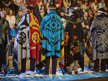 Five Indigenous Role Models blanketed and stand in the longhouse in front of their peers