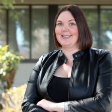 Woman with short brown hair wearing black leather jacket poses for photo