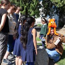 Female secondary student reads book inspired by elementary student artwork as others listen