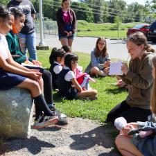 Female secondary student reads book inspired by elementary student artwork as others listen