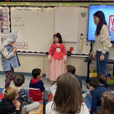 Elementary students sitting on floor learning from a family about traditional Asian attire.