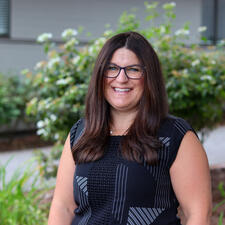 Professional Headshot of female employee. Picture is taken outside with a building in the background.